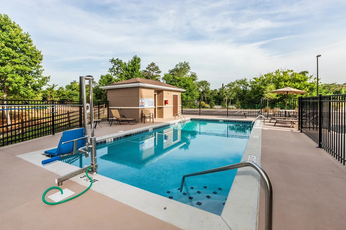 This exterior image highlights the hotel's seasonal outdoor pool surrounded by poolside lounge chairs, with an accessibility lift and a pool house in view. The setting is lively and inviting, suitable for socializing, relaxing, or participating in poolside activities, and is accentuated by bright natural light.