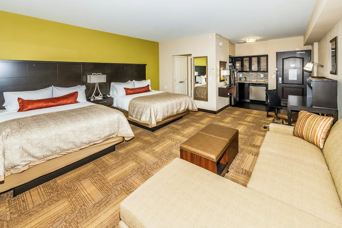 A bright, inviting studio featuring two plush queen beds with decorative pillows, a cozy sitting area for morning coffee or evening chats, and a convenient workspace, all set in a modern, comfortable layout.