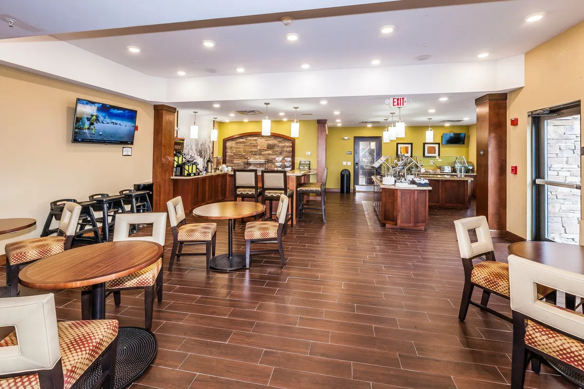 A comfortable interior with tables and chairs set for dining, a bar area, a counter display, a TV screen, and decorative stone-accented walls. The scene reflects a relaxed and casual atmosphere suited for shared meals and friendly gatherings.