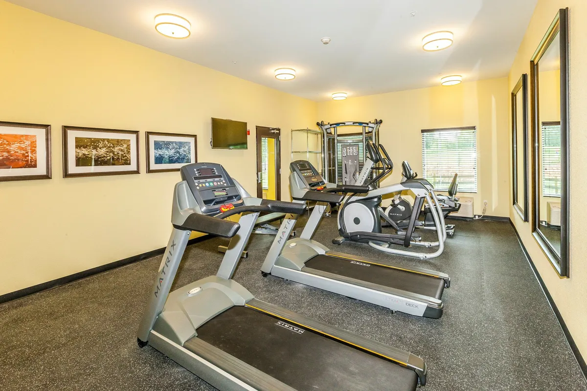 A modern fitness center with treadmills, elliptical machines, weight training equipment, large mirrors, and framed art on the walls. The space is bright and motivating, designed to help guests maintain wellness during their stay.
