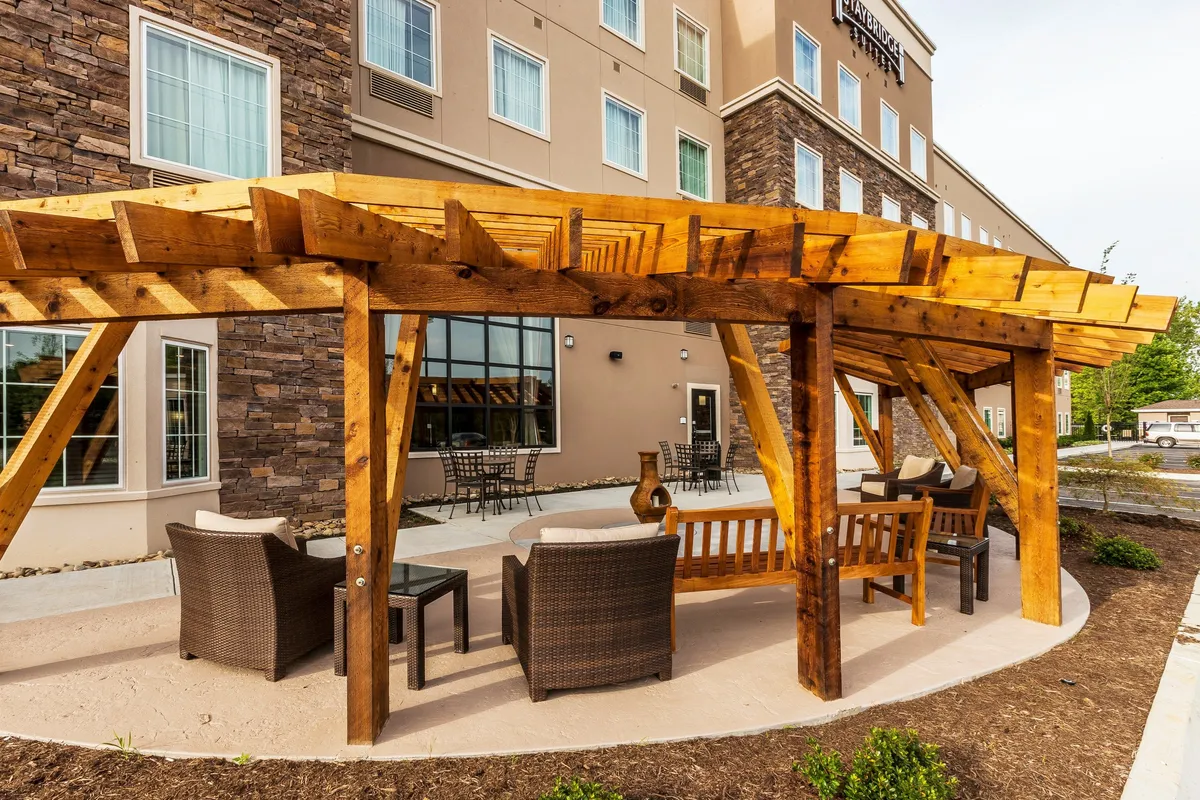 Featuring a wooden pergola over outdoor seating adjacent to a stone façade, this image evokes a comfortable, social atmosphere. Guests can imagine themselves relaxing outdoors, enjoying a morning coffee or an evening with friends after exploring the nearby district.