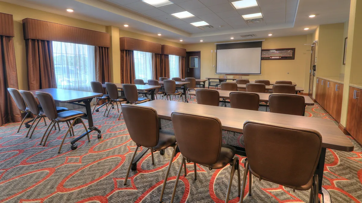 An interior scene showing tables and chairs arranged for meetings, with a presentation screen at the front, creating a productive and collaborative environment perfect for business meetings, training sessions, or workshops.